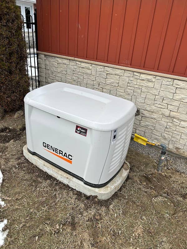 A Generac standby generator on a concrete pad against a stone wall, with the yellow gas line and its shutoff visible at the side of the cabinet